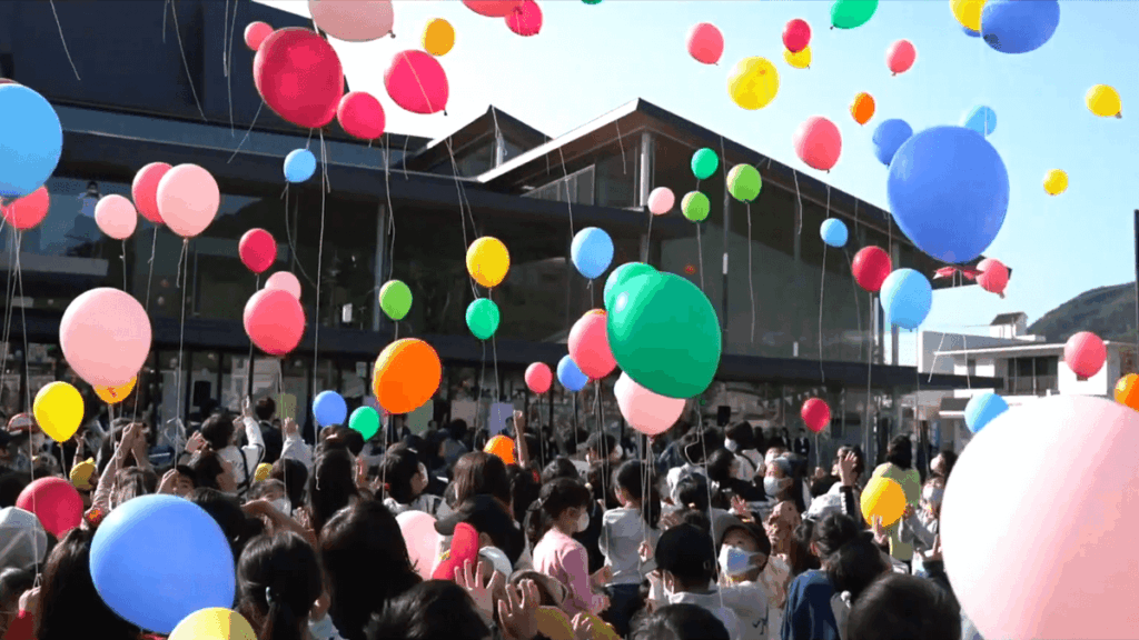 さいき城山桜ホールに集まった市民の手から一斉に風船が空に放たれる様子
