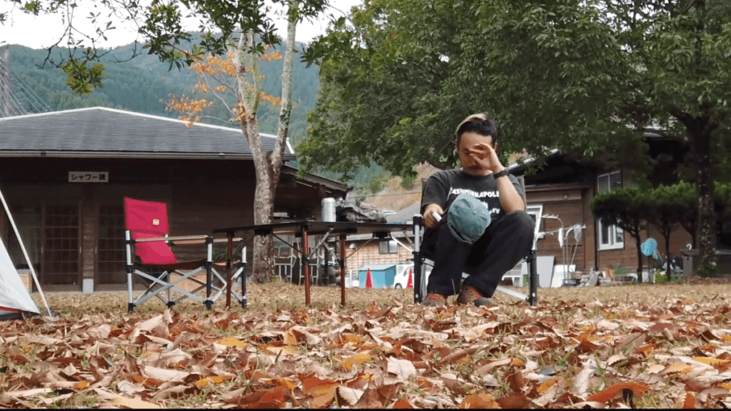 落ち葉に囲まれた大分県佐伯市うめむらキャンプ場で椅子に座る男性