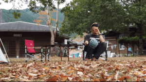 落ち葉に囲まれた大分県佐伯市うめむらキャンプ場で椅子に座る男性